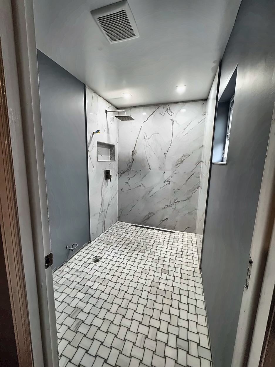 The finished walk-in shower with marble-look slab walls, basketweave mosaic floor, rain head and linear drain