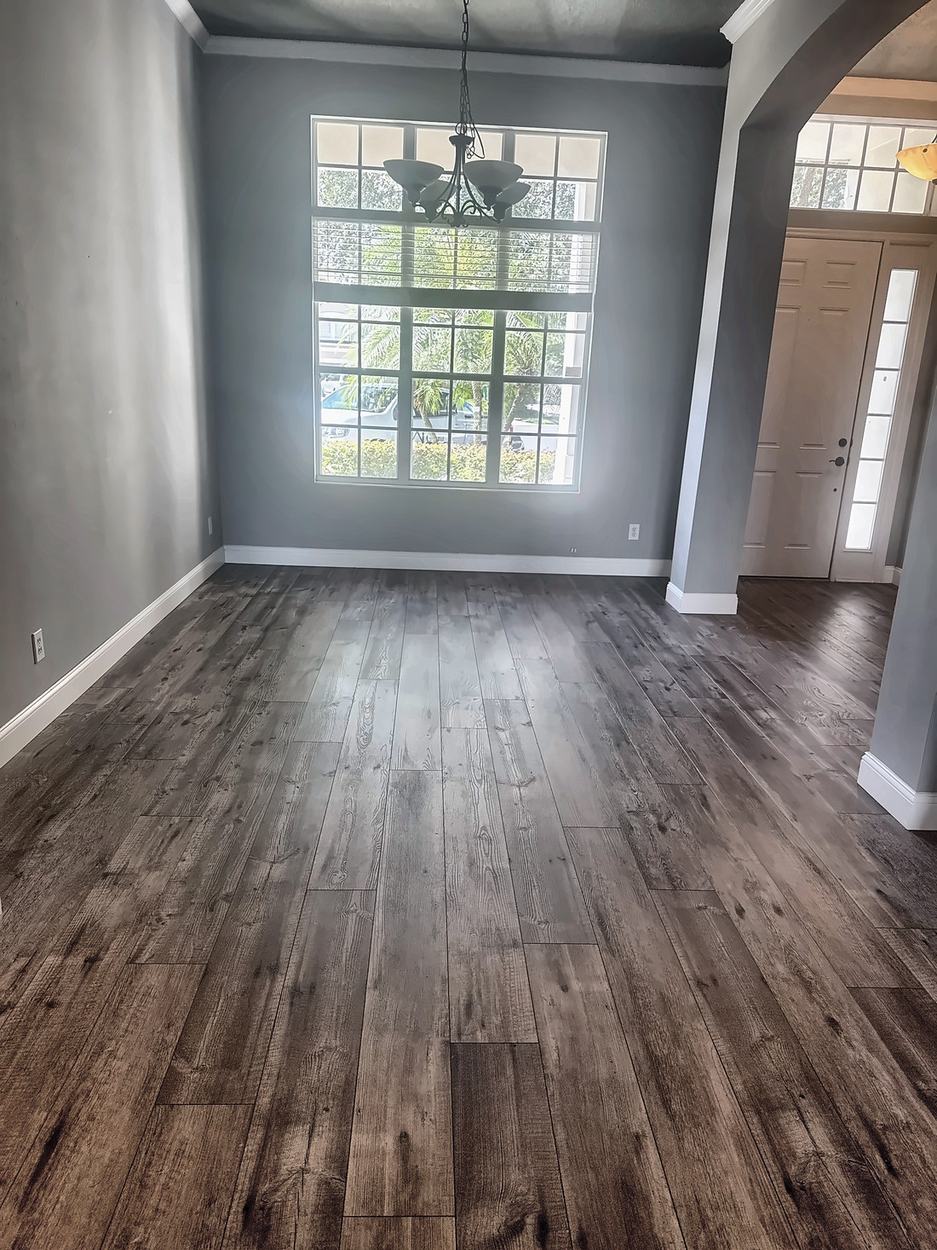 Dining room before renovation: an empty grey room with a tall multi-pane window, a wrought iron chandelier and an arched opening beside the front door