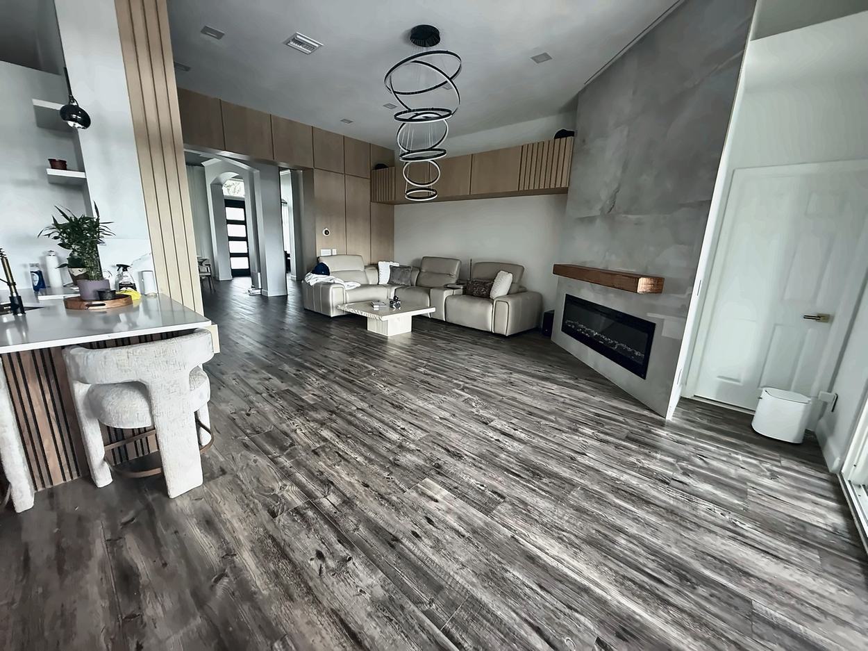 The same open plan after renovation: fluted timber column at the kitchen peninsula, full-height oak cabinetry the length of the room, sculptural ring chandelier and the plaster fireplace slab at right