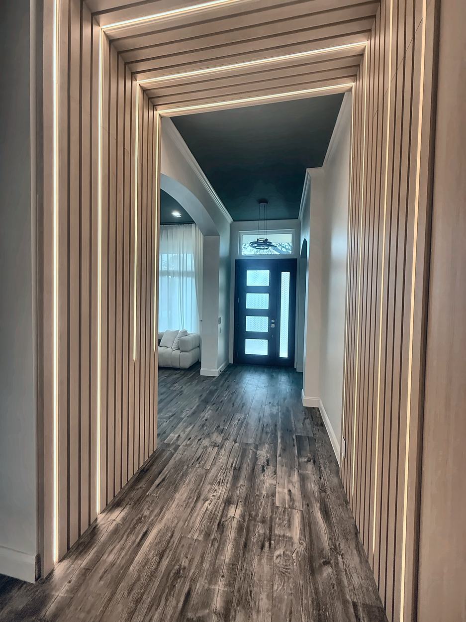 Hallway framed by a fluted timber portal with concealed LED strips set between the fins, looking through to the navy front door