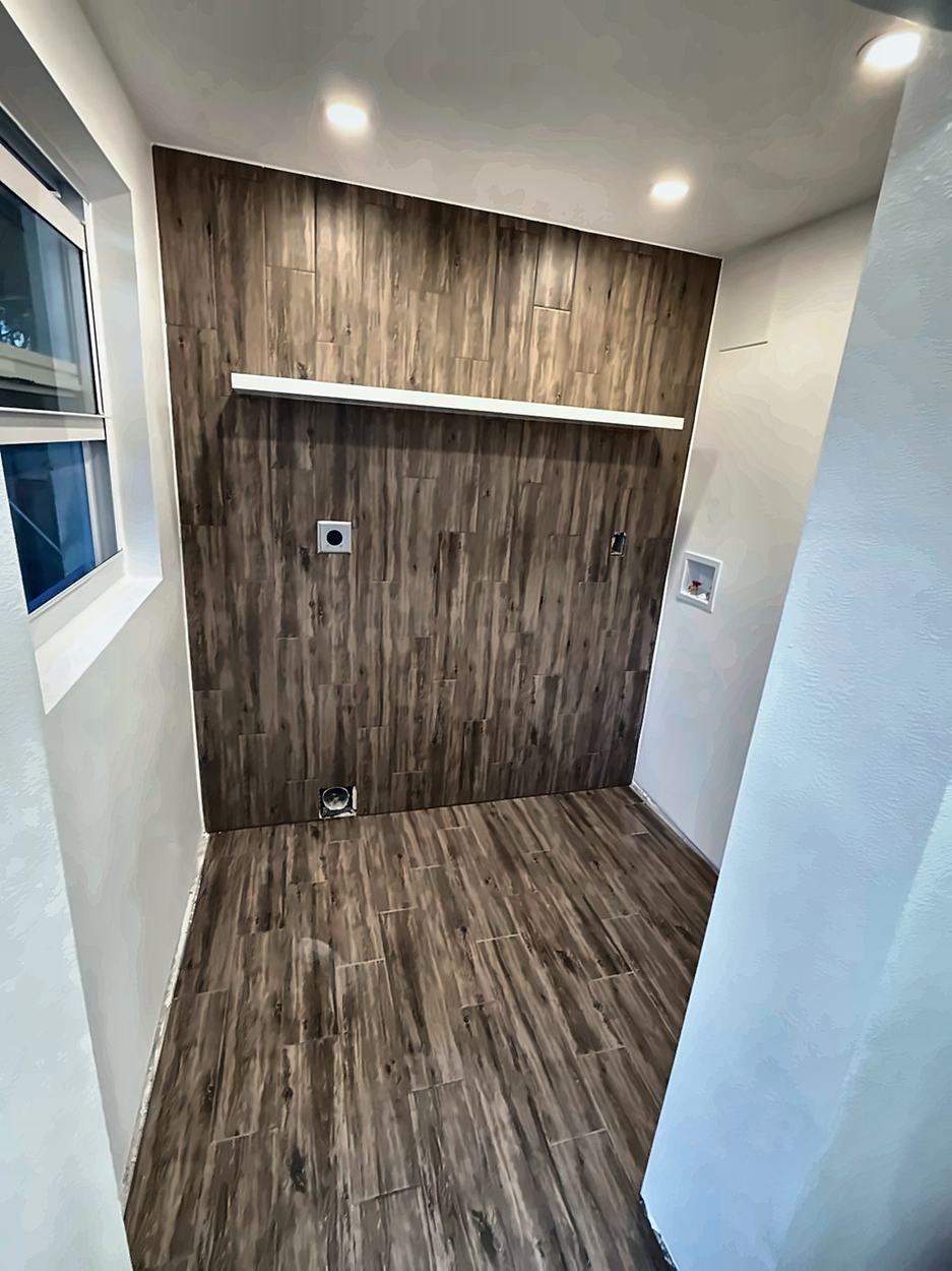Finished laundry room with wood-look plank tile on wall and floor, a floating shelf and recessed hookups