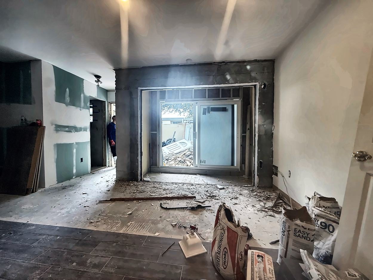 Gutted living area mid-demolition with a new slider opening cut into the block wall