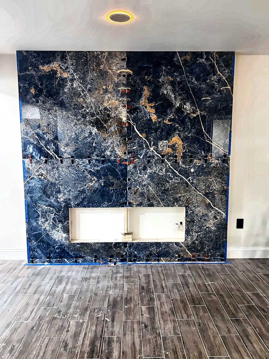 Large-format blue and gold marble-look slab being set with leveling clips still in place
