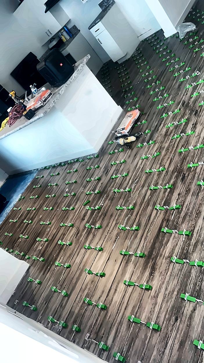 Wood-look porcelain plank tile being installed with green leveling clips