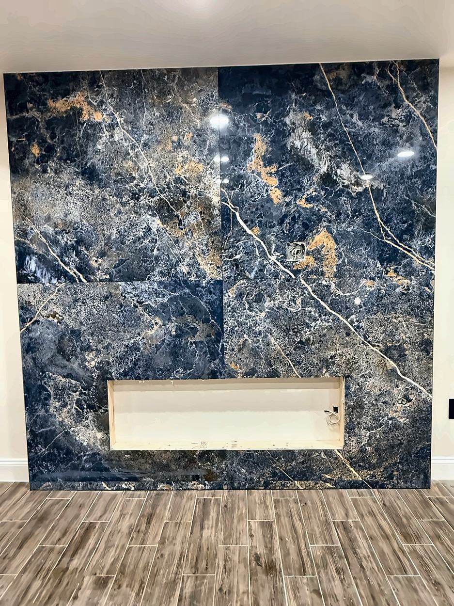 A floor-to-ceiling feature wall in blue and gold book-matched stone slab, with the linear fireplace opening cut and framed, photographed before the unit is installed